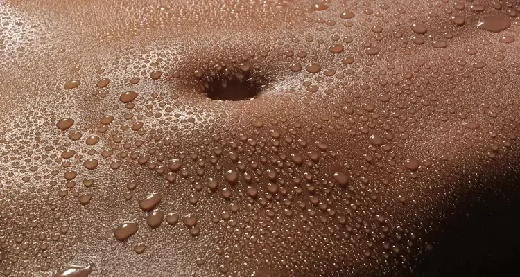 Close-up of a stomach with numerous water droplets, some forming a small puddle around the belly button.