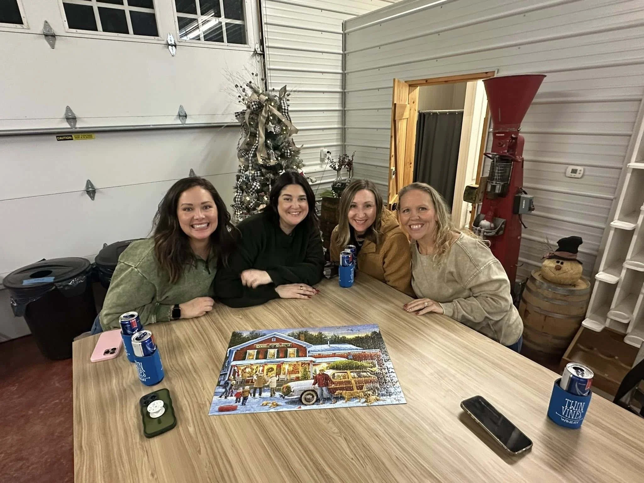 2025 Holiday puzzle night at Twin Vines. Group of four women smiling around a table with a finished Christmas puzzle and Mcultras.