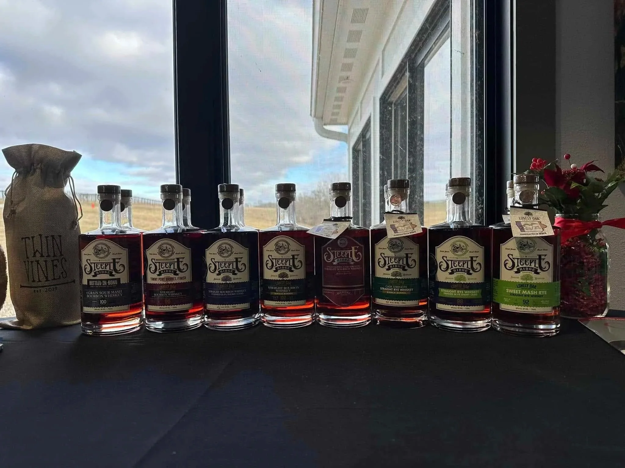 8 bourbon flavors lined up on black tablecloth in front of window.