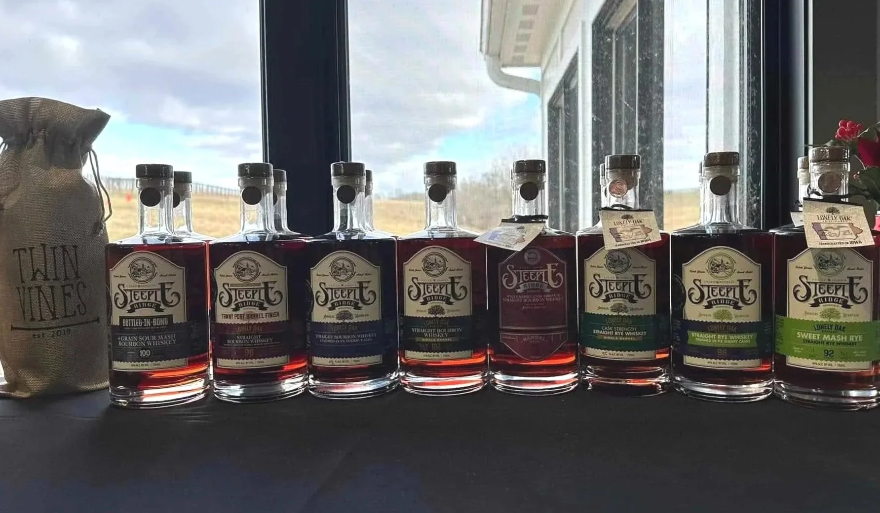 Craft bourbon offered at Twin Vines in Panora Iowa.  8 bourbon flavors lined up on black tablecloth in front of window.