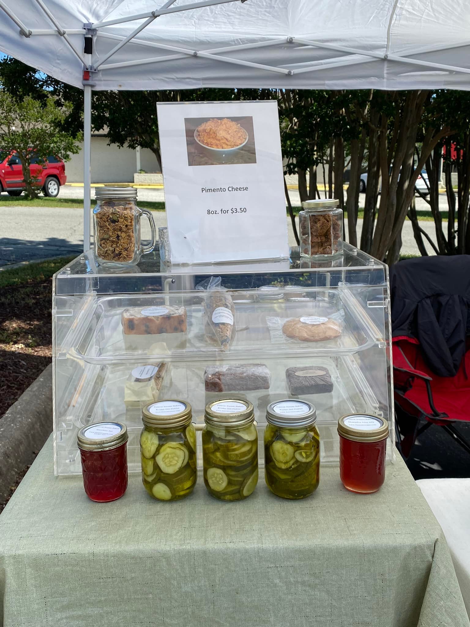 Market stall with pimento cheese sign, jars of pickles and jams, and assorted baked goods under a canopy.