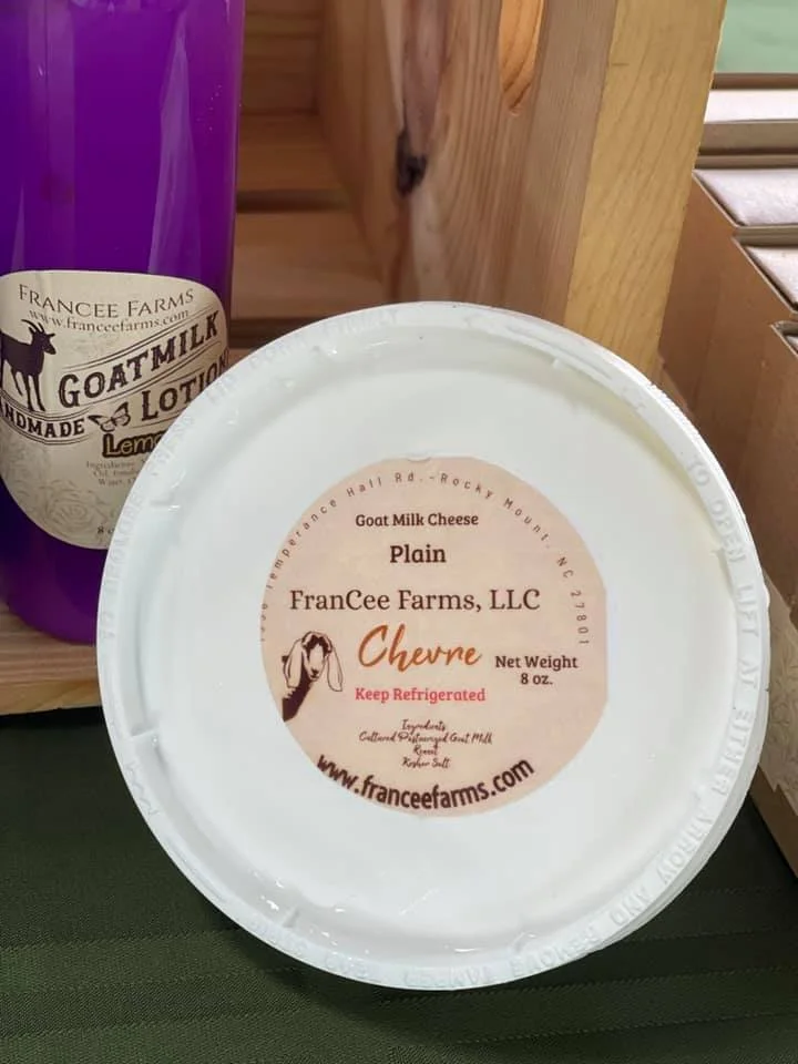 Goat milk cheese from FranCee Farms next to a bottle of goat milk lotion on a wooden surface.