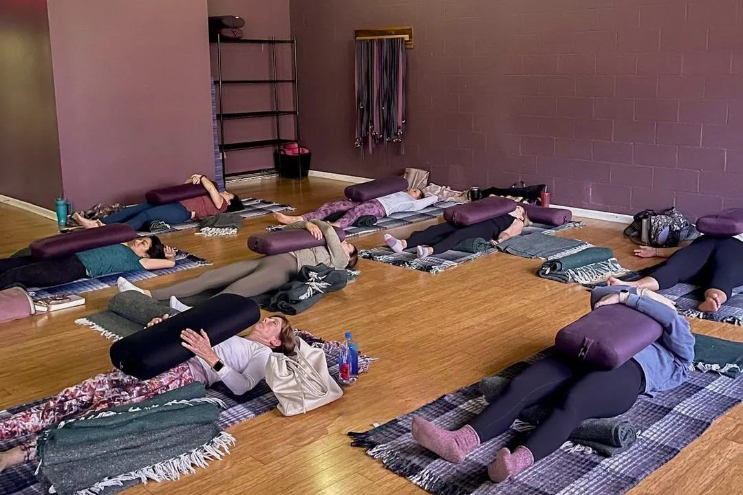 Restorative yoga class with students lying on mats supported by bolsters in a calm studio setting at Prana Yoga Center