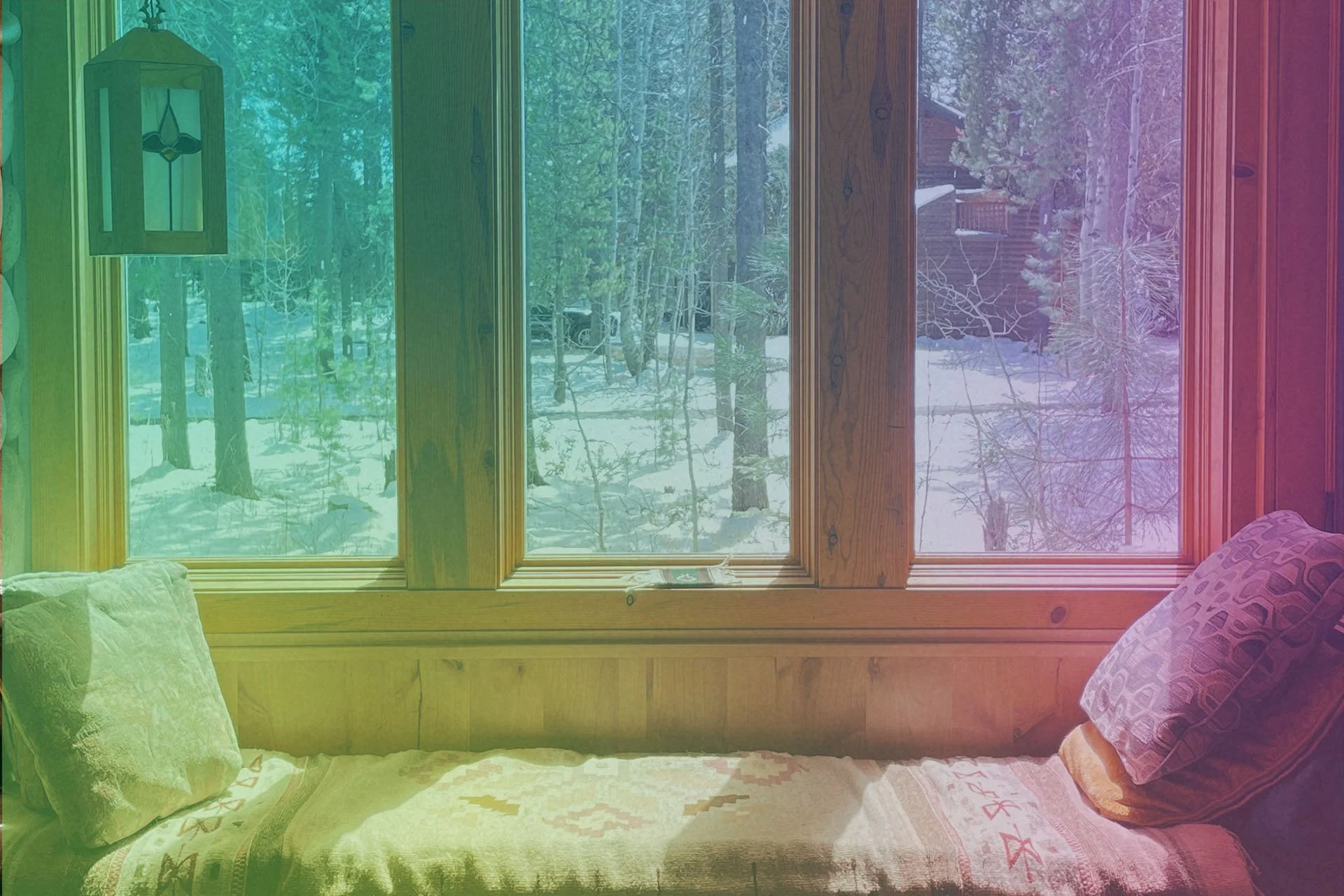 Soft winter light fills a quiet interior window seat, with snow-covered trees visible outside, creating a sense of warmth and rest.