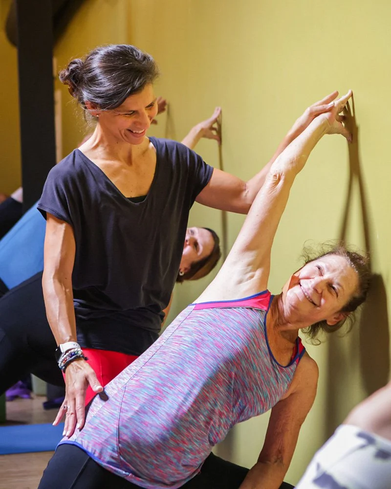 Kathryn Carr gently assisting a student in a supported side stretch during a yoga class at Prana Yoga Center in Geneva, Illinois.