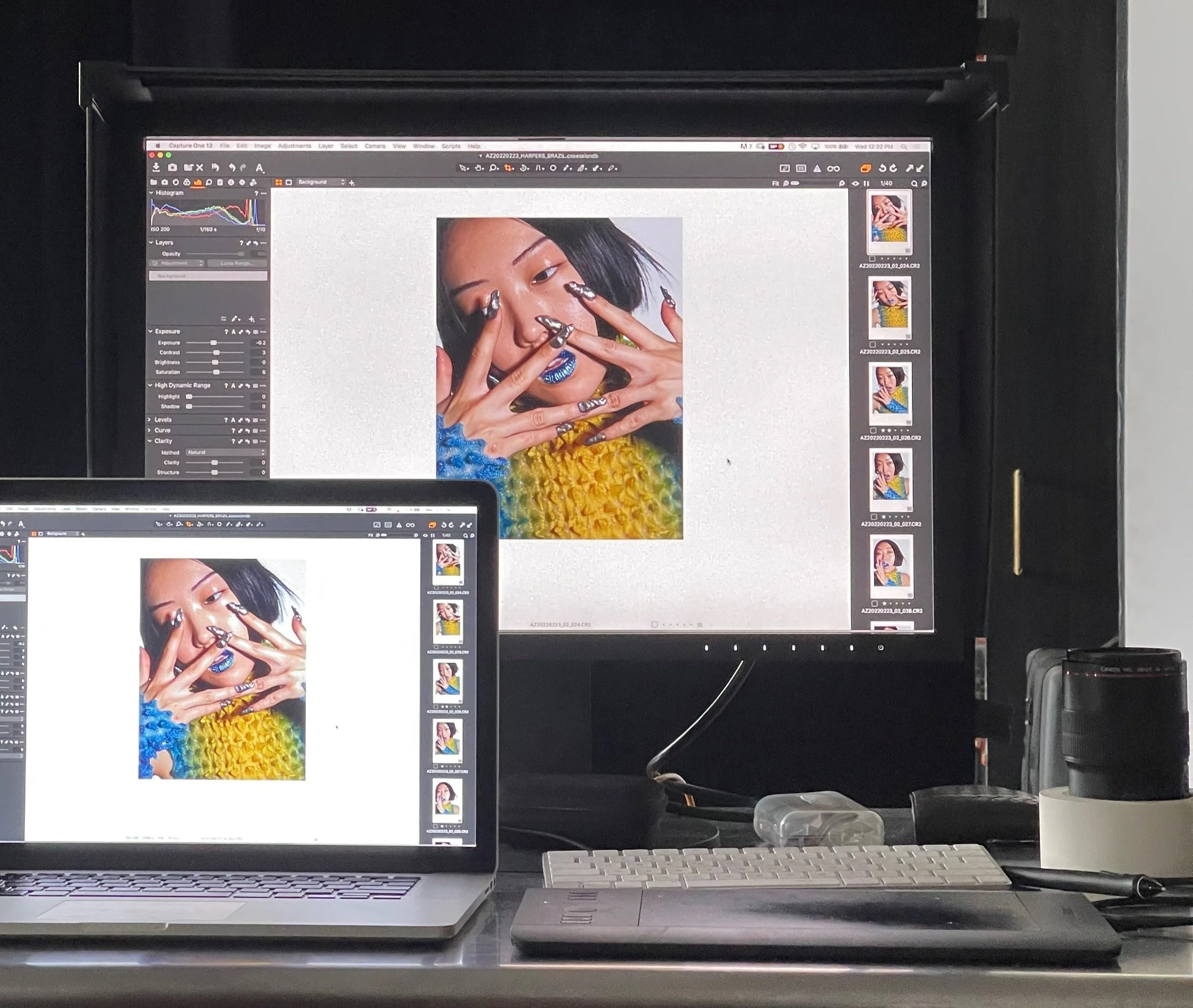 A dual-monitor computer setup displaying a color photo of a woman with black hair, bright makeup, and colorful clothing. The main monitor shows a photo editing or graphic design application, while the smaller laptop screen displays the same image with a photo strip on the side.