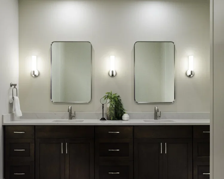 Double vanity with dark wood cabinets, twin mirrors and wall sconces