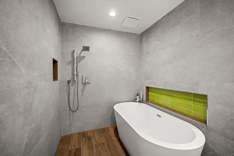 Walk-in shower with gray tile, green tile niche and freestanding tub