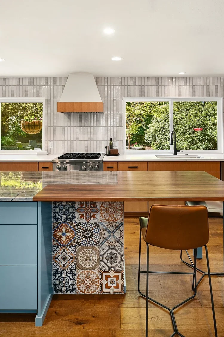 Blue kitchen island with patterned tile, white range hood and bar stools