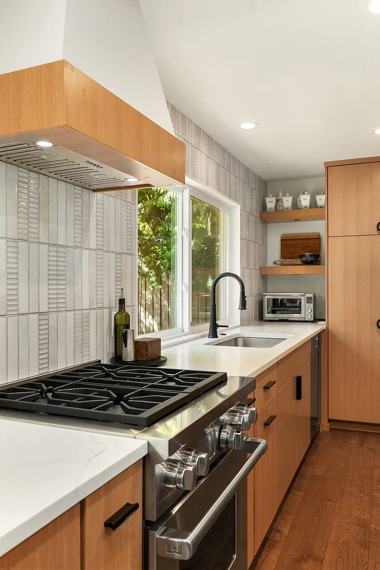 Gas range with white tile backsplash and wood cabinets beside a window