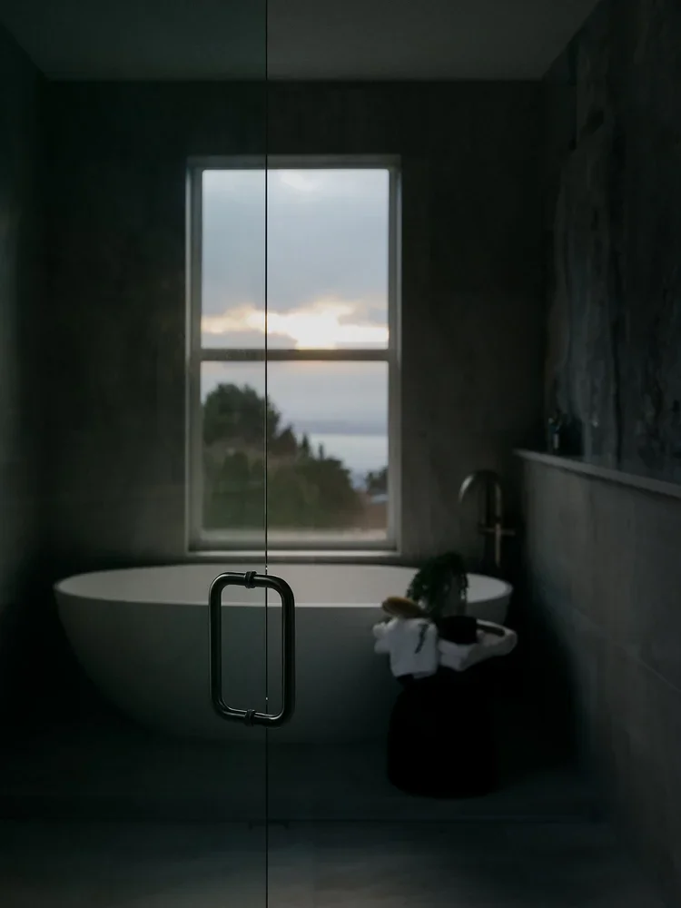Freestanding soaking tub under a window in a dark-toned bathroom