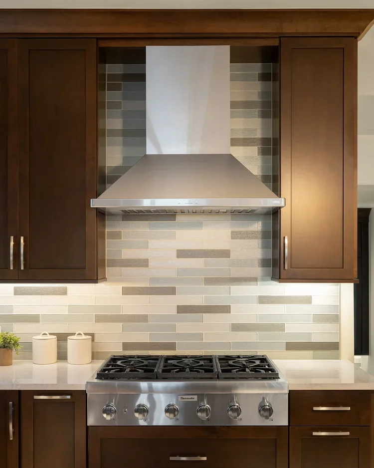 Stainless range hood with stone-look tile backsplash and dark wood cabinets