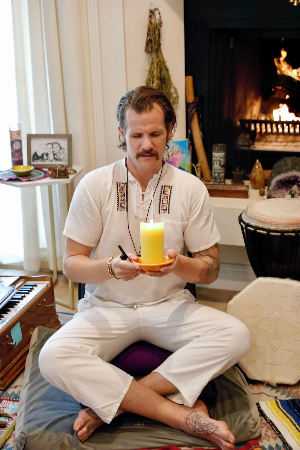 Clark is banging a drum in ceremonial clothing in front of a creek.