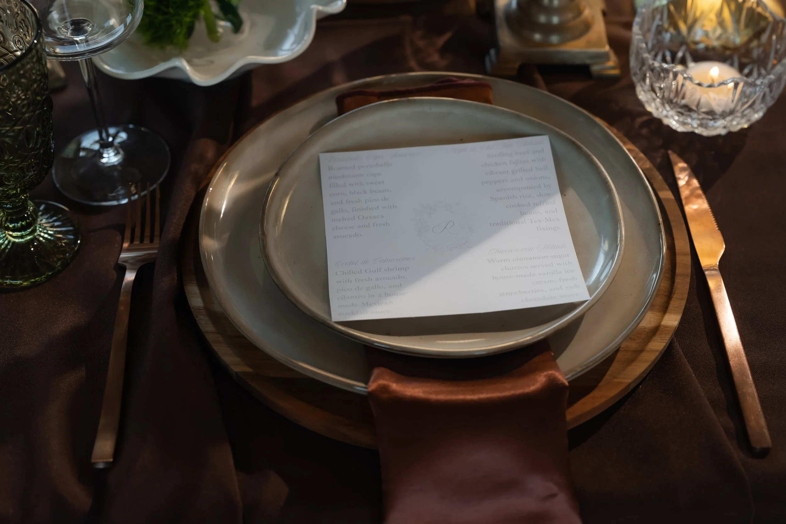 Wedding place setting with a printed menu, layered plates and glassware.