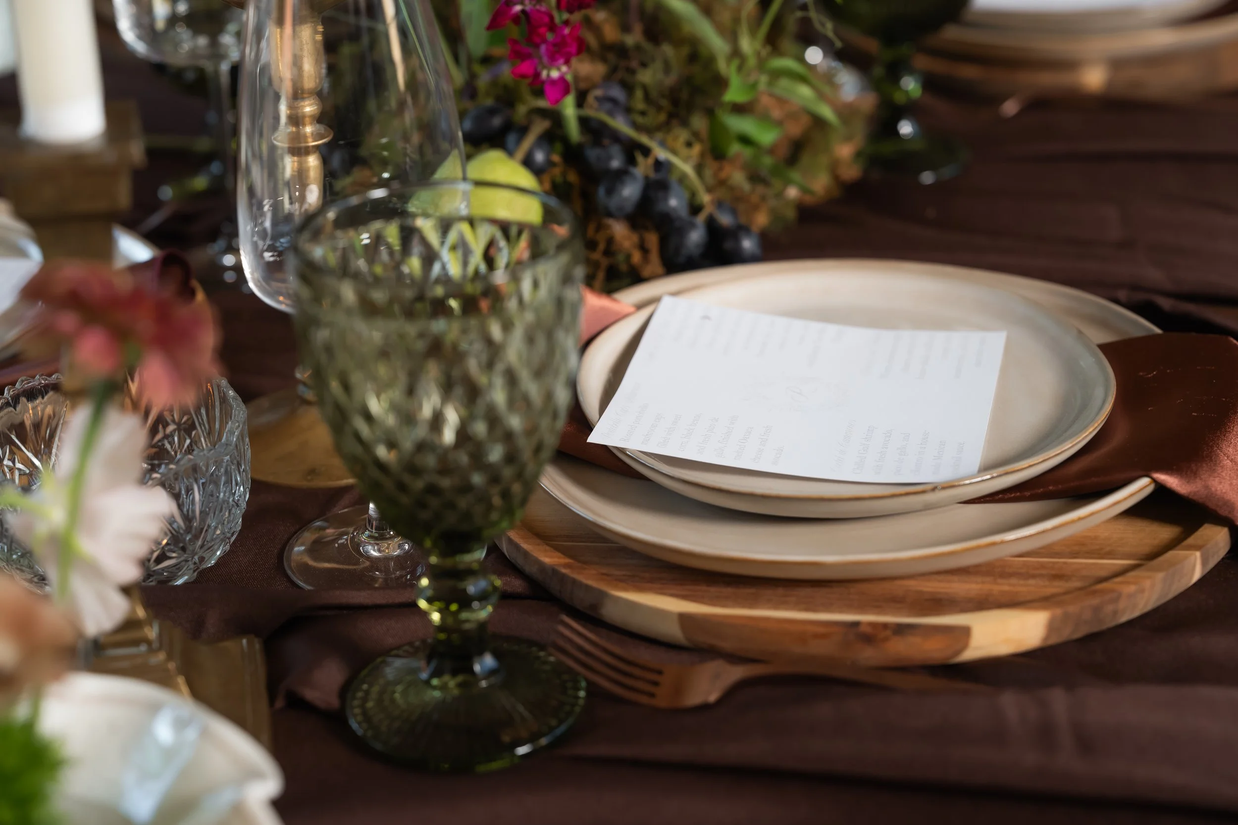 Wedding place setting with crystal glassware, a menu and floral arrangements.