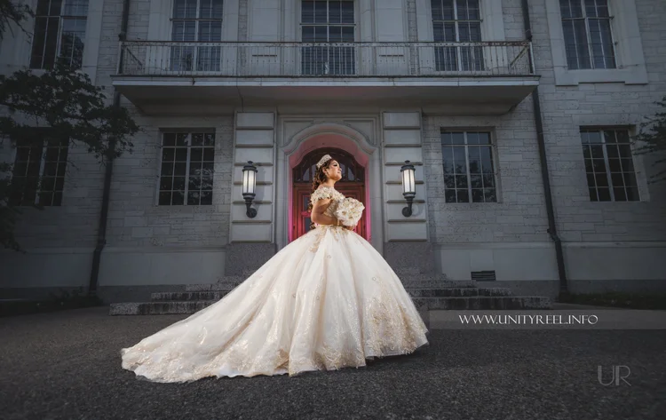 Portrait of a woman in a white gown holding flowers in front of a building.