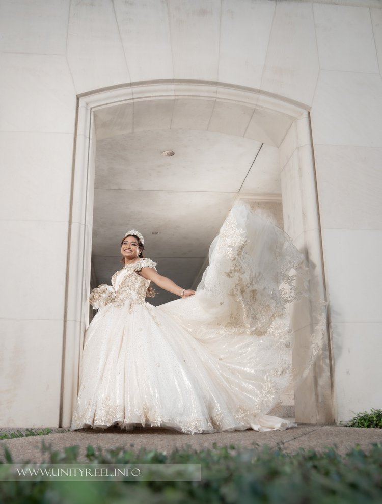 Portrait of a woman smiling and holding the train of her gown beneath an archway.