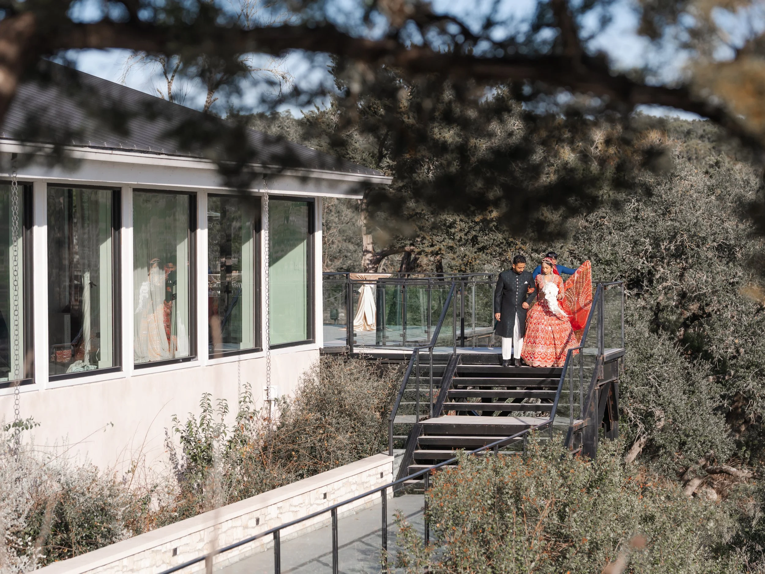 A bride dressed in traditional Indian wedding attire walking on a balcony overlooking trees and greenery on the Terrace at the Videre Estate during the processional for her wedding ceremony.