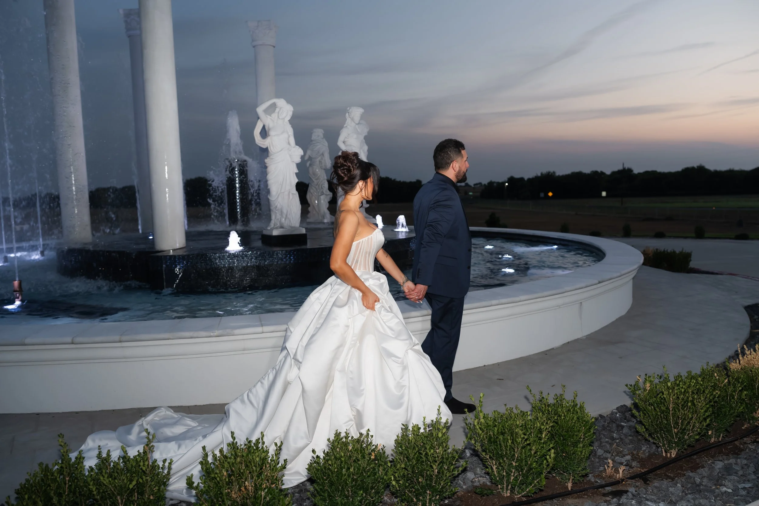 Bride and groom beside an estate fountain in the last light of sunset