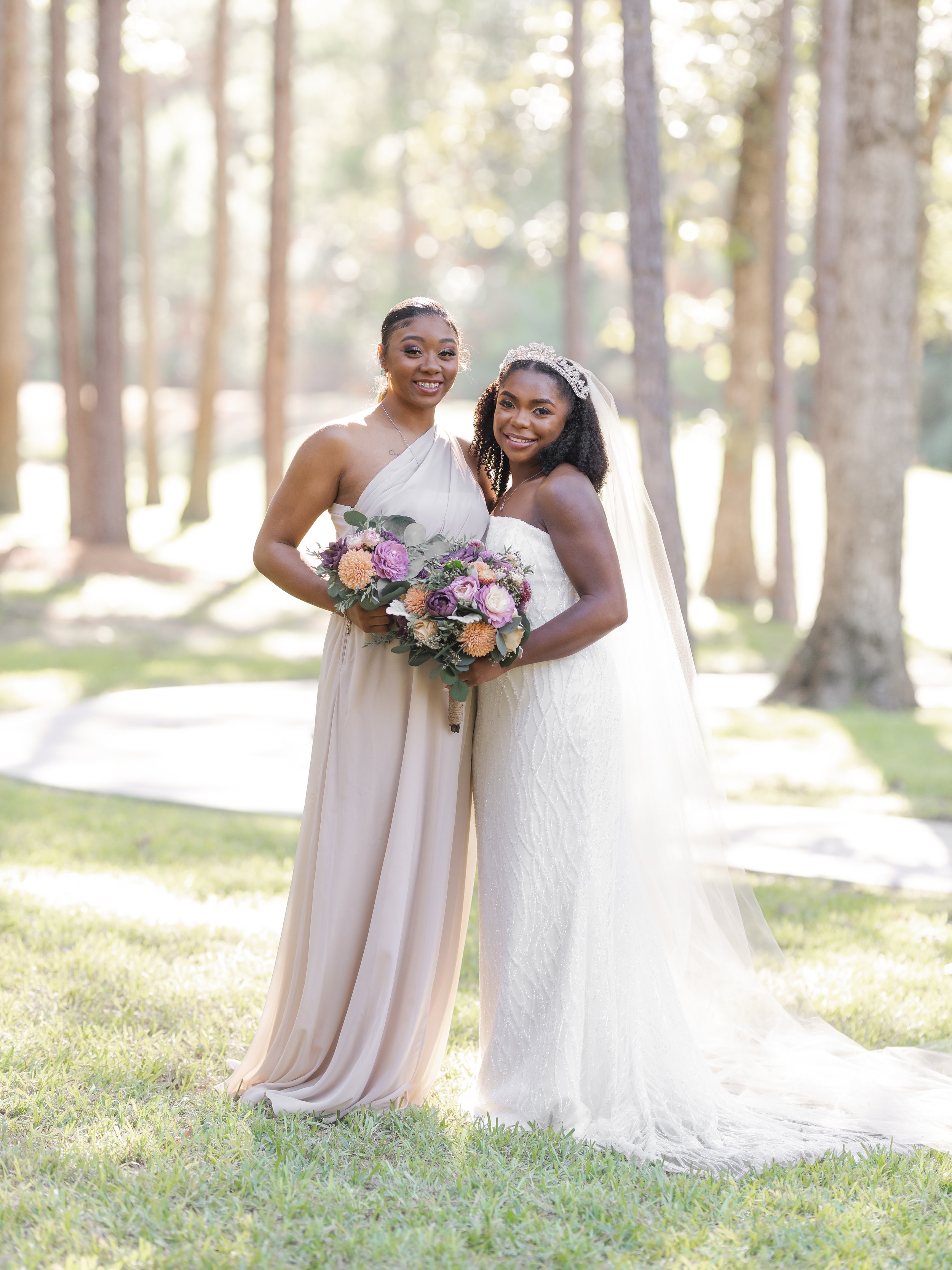 Beautiful bride standing next to her bridesmaid with the sun glowing and illuminating the trees behind them at Springs Event Venue