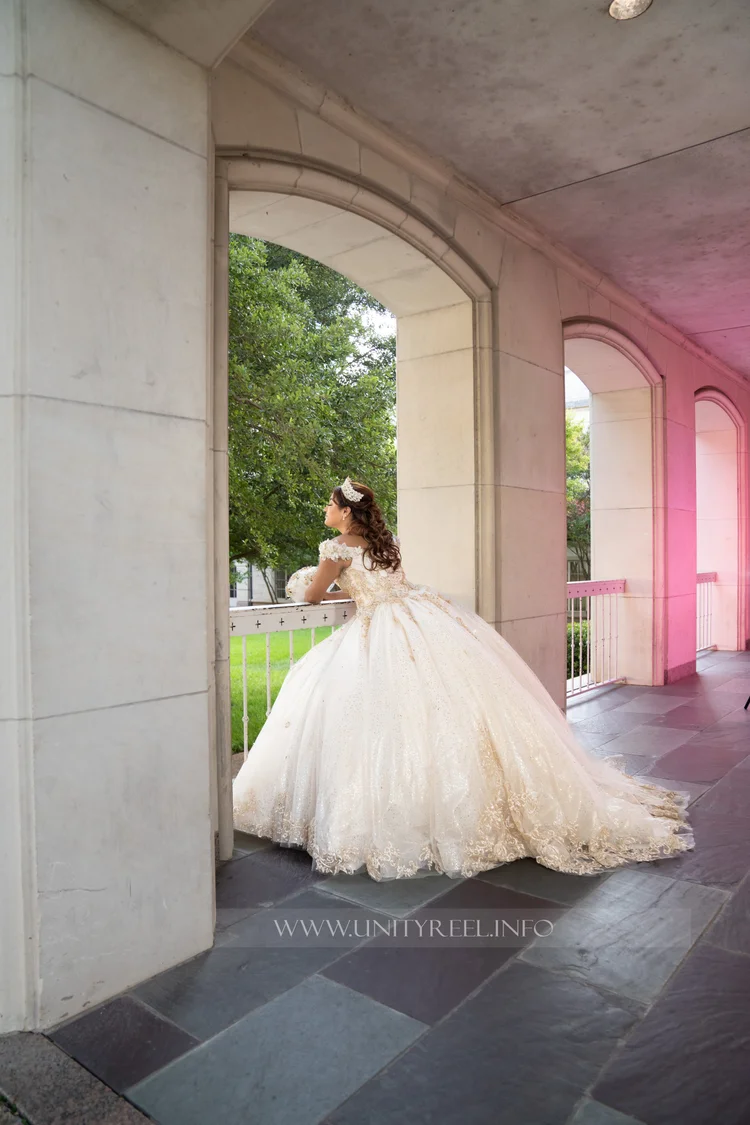 Portrait in a lace-embellished white gown, with hands resting on a balcony railing overlooking trees.