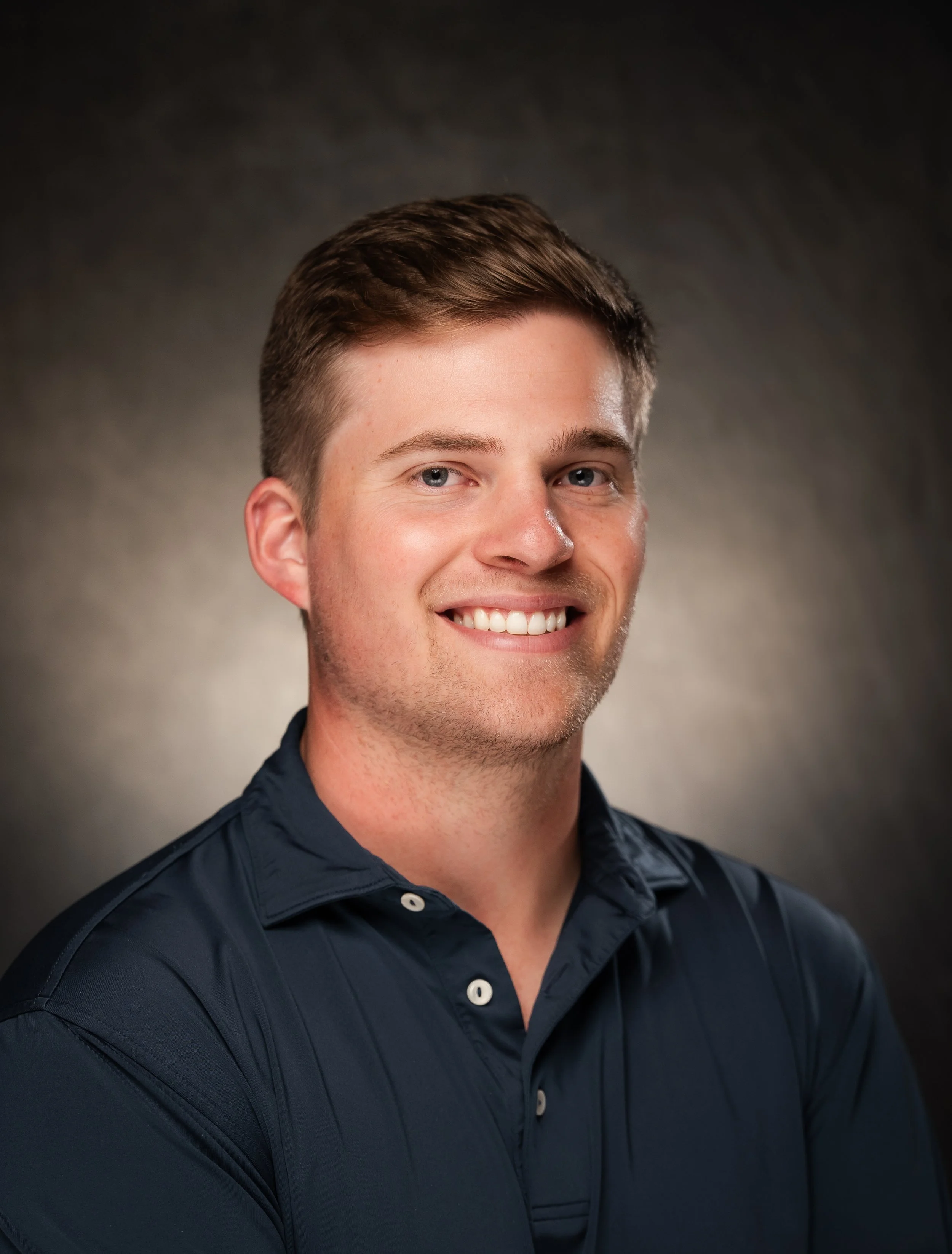 Smiling man in a navy shirt posed for a professional headshot.