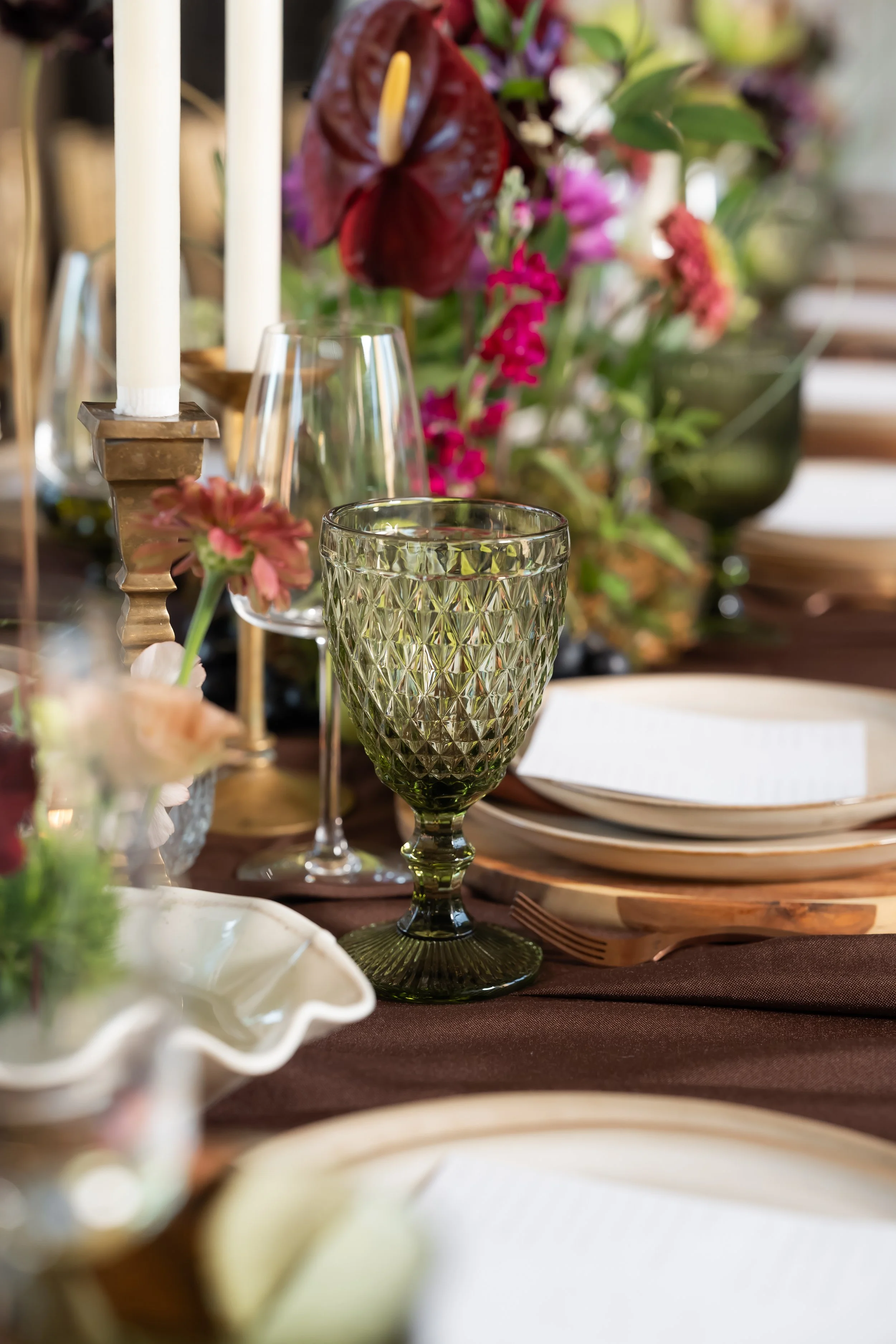 Wedding table with green glassware, flowers and white candles.