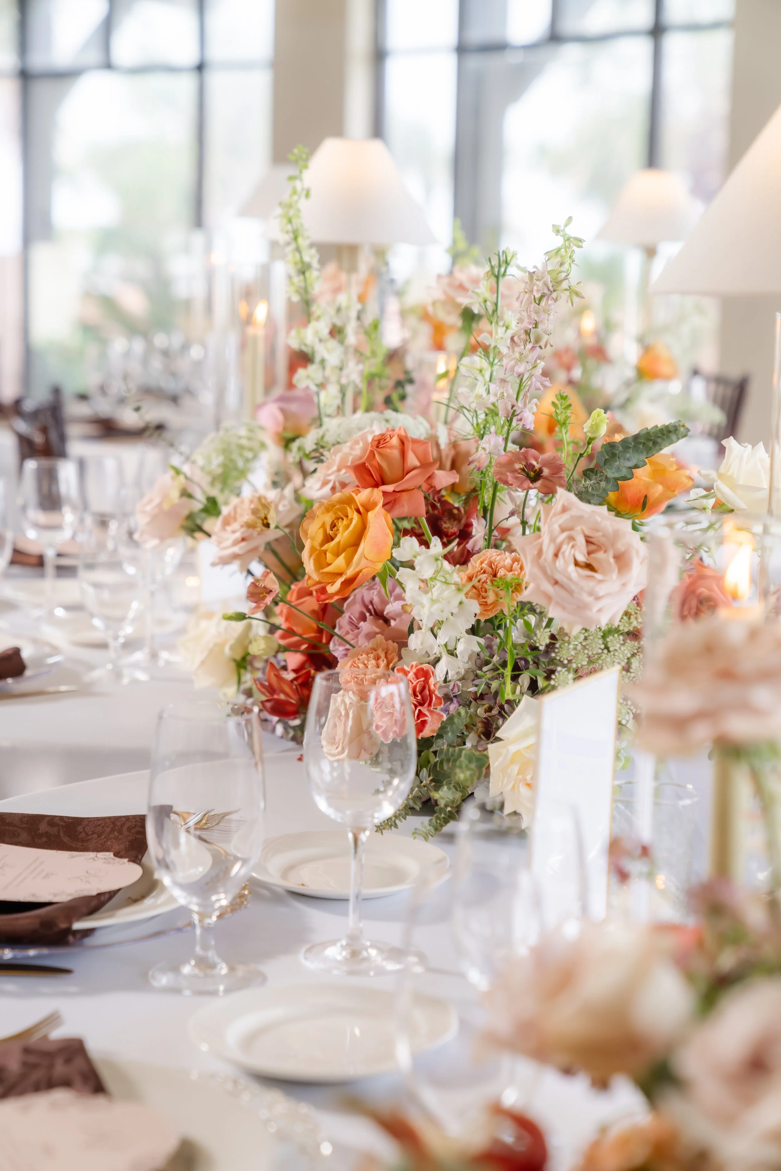 Elegant dining table decorated with a large floral centerpiece consisting of pastel-colored roses, orchids, and greenery, with wine glasses, plates, and candles in the background in the reception space at the Grand Galvez Hotel in Galveston.