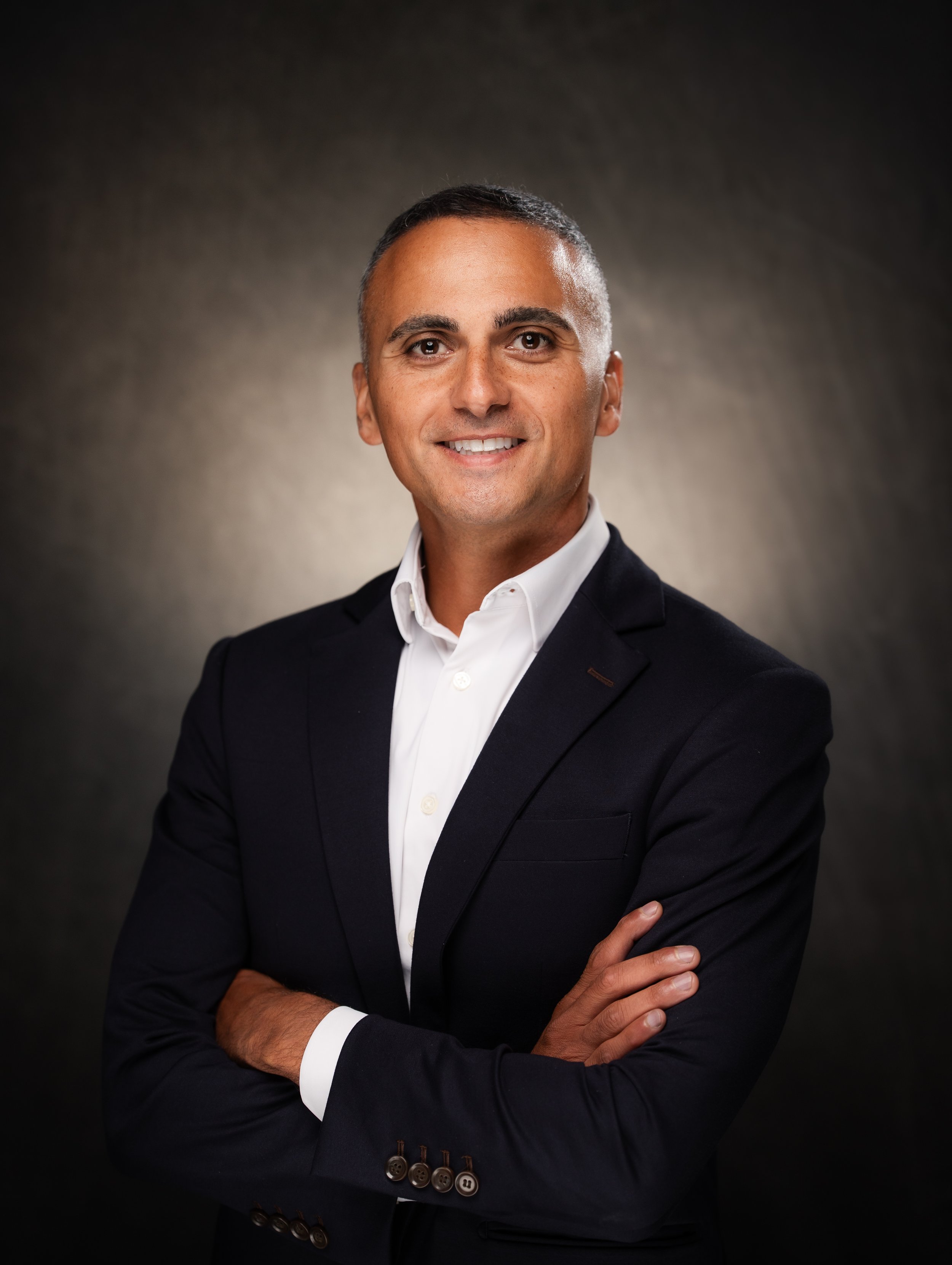 Professional portrait of a man in a black suit and white shirt with arms crossed.