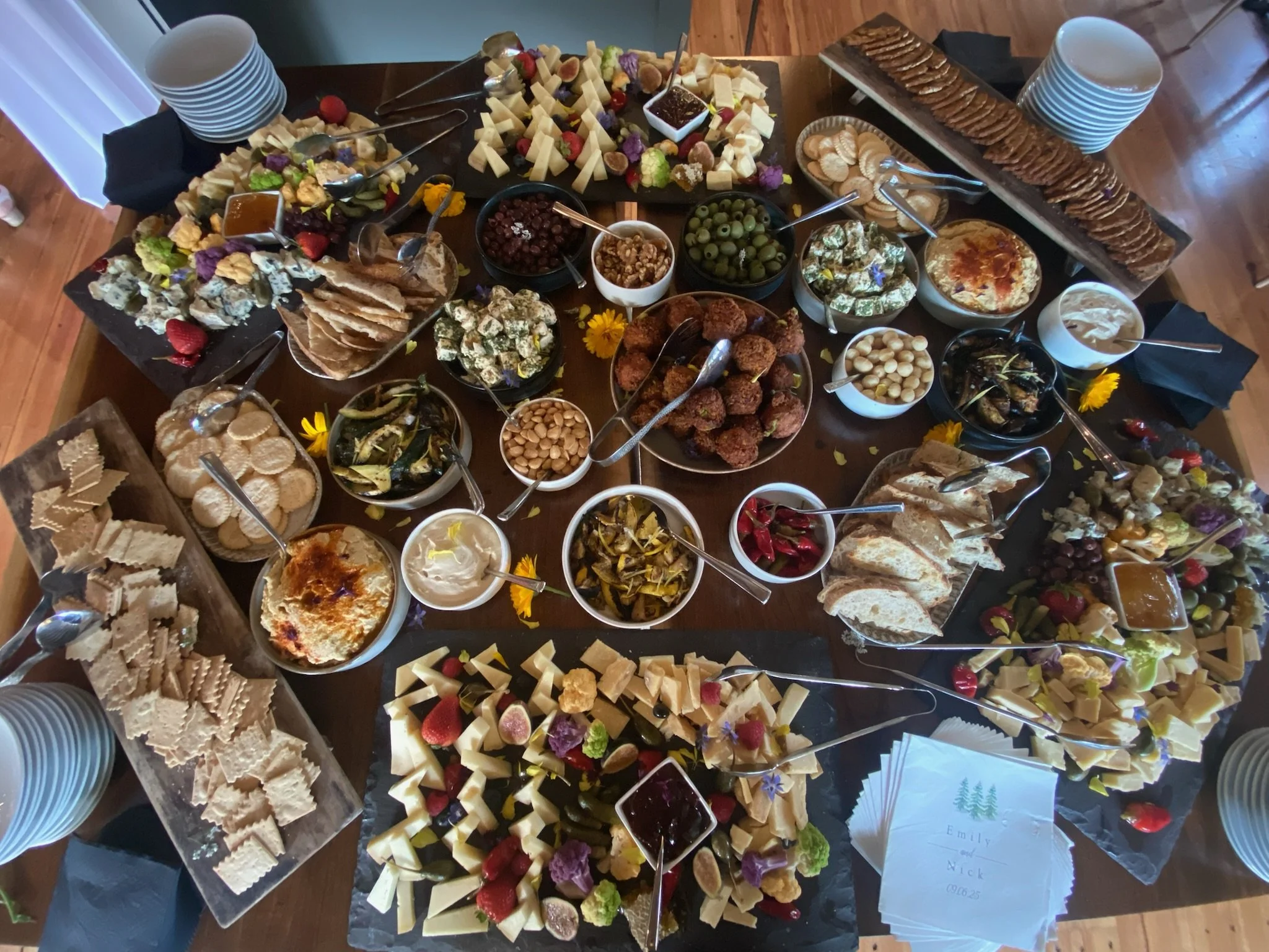 A large assortment of cheese, crackers, grapes, nuts, dips, and assorted finger foods arranged on a table for a gathering.