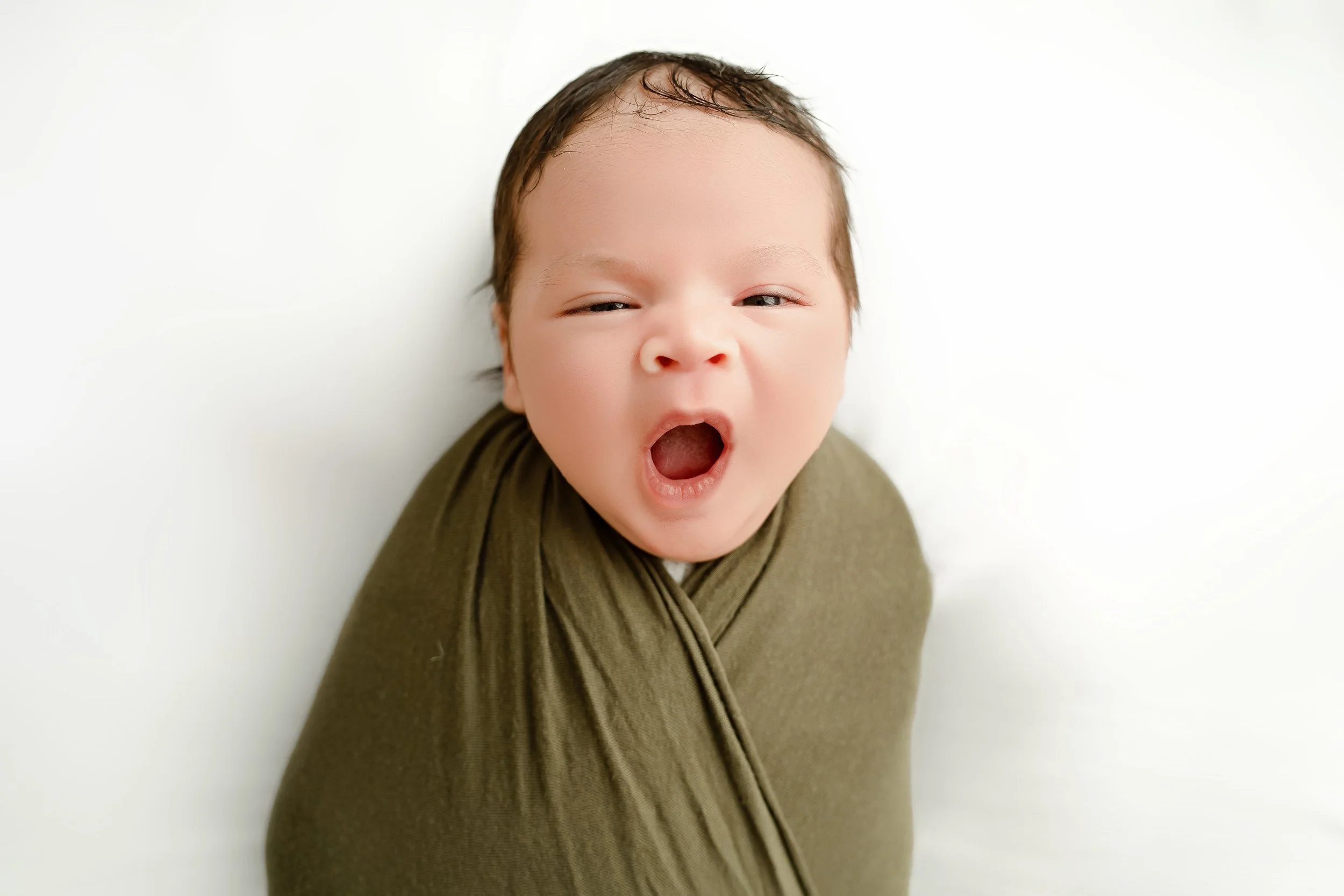 A baby yawning while wrapped in a green cloth