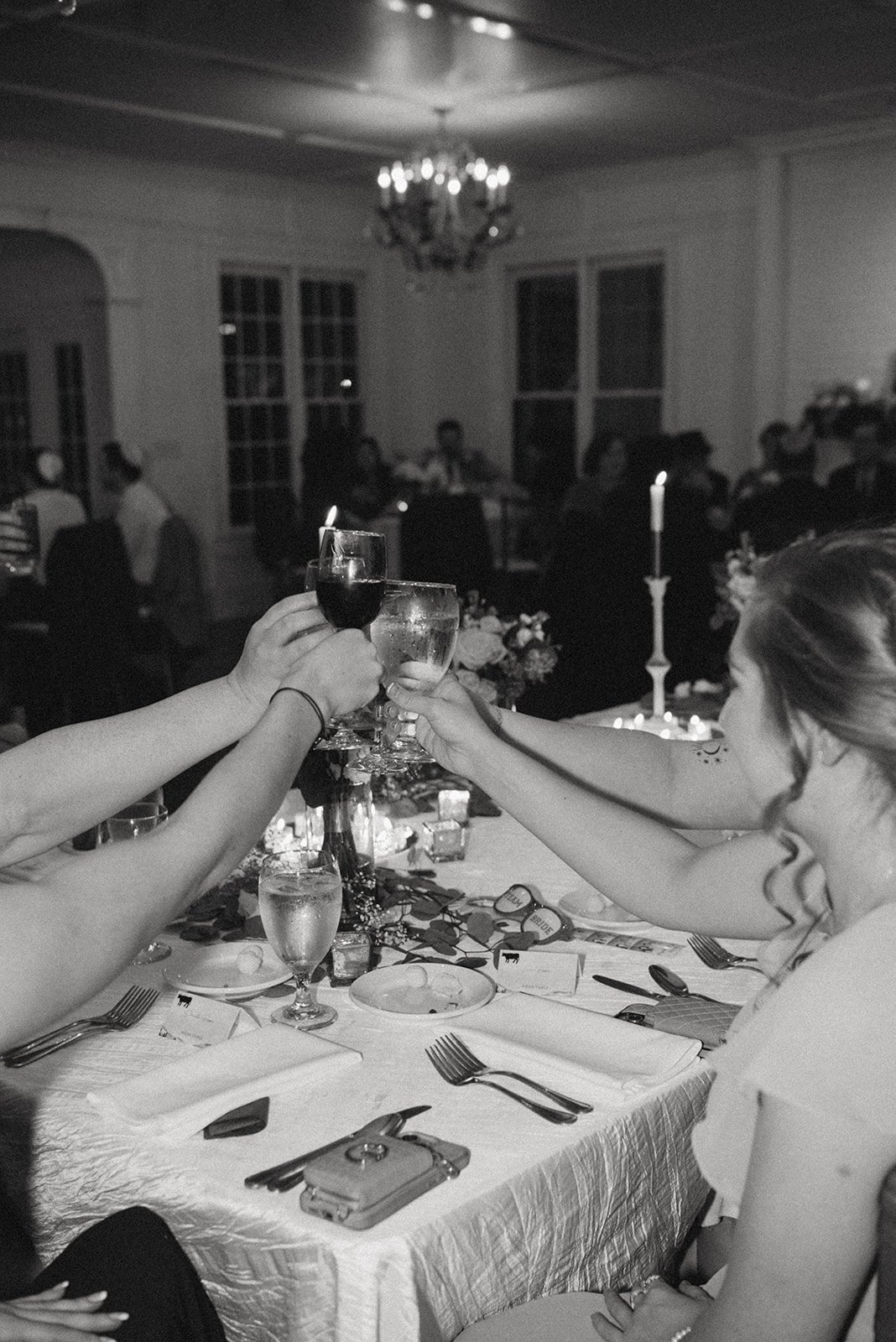 People at a dinner table raising glasses in a toast during a celebration in a decorated dining room with a chandelier and candles.