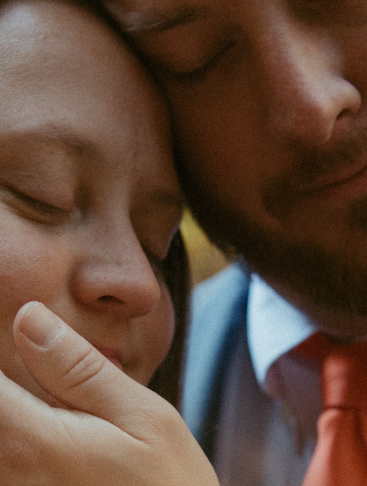 Close-up of two people with their foreheads touching, one with closed eyes and asians and the other with dark skin with closed eyes, with a finger touching the face of the Asian person.