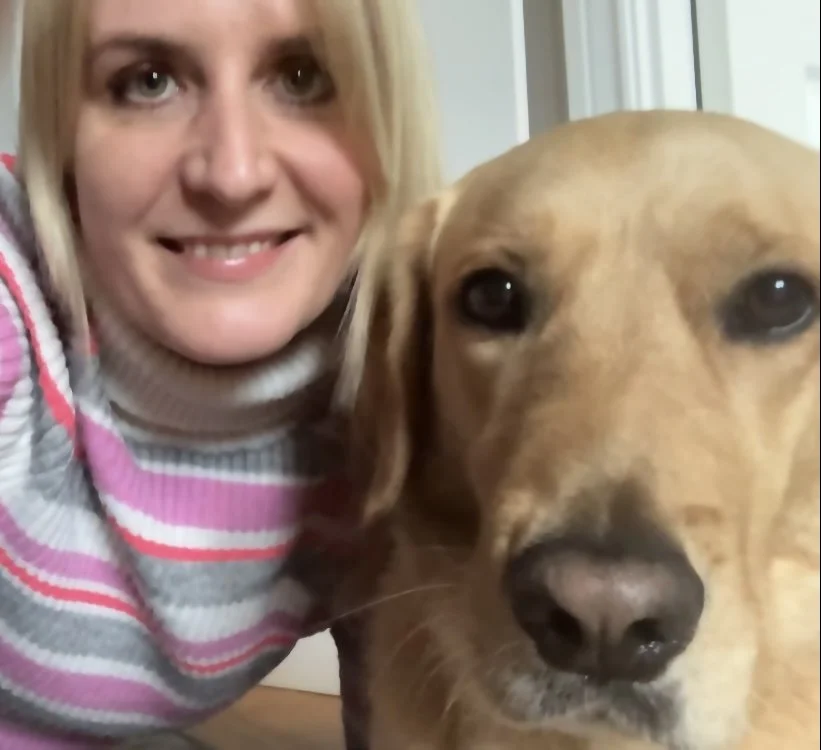 A woman smiling next to a golden dog.