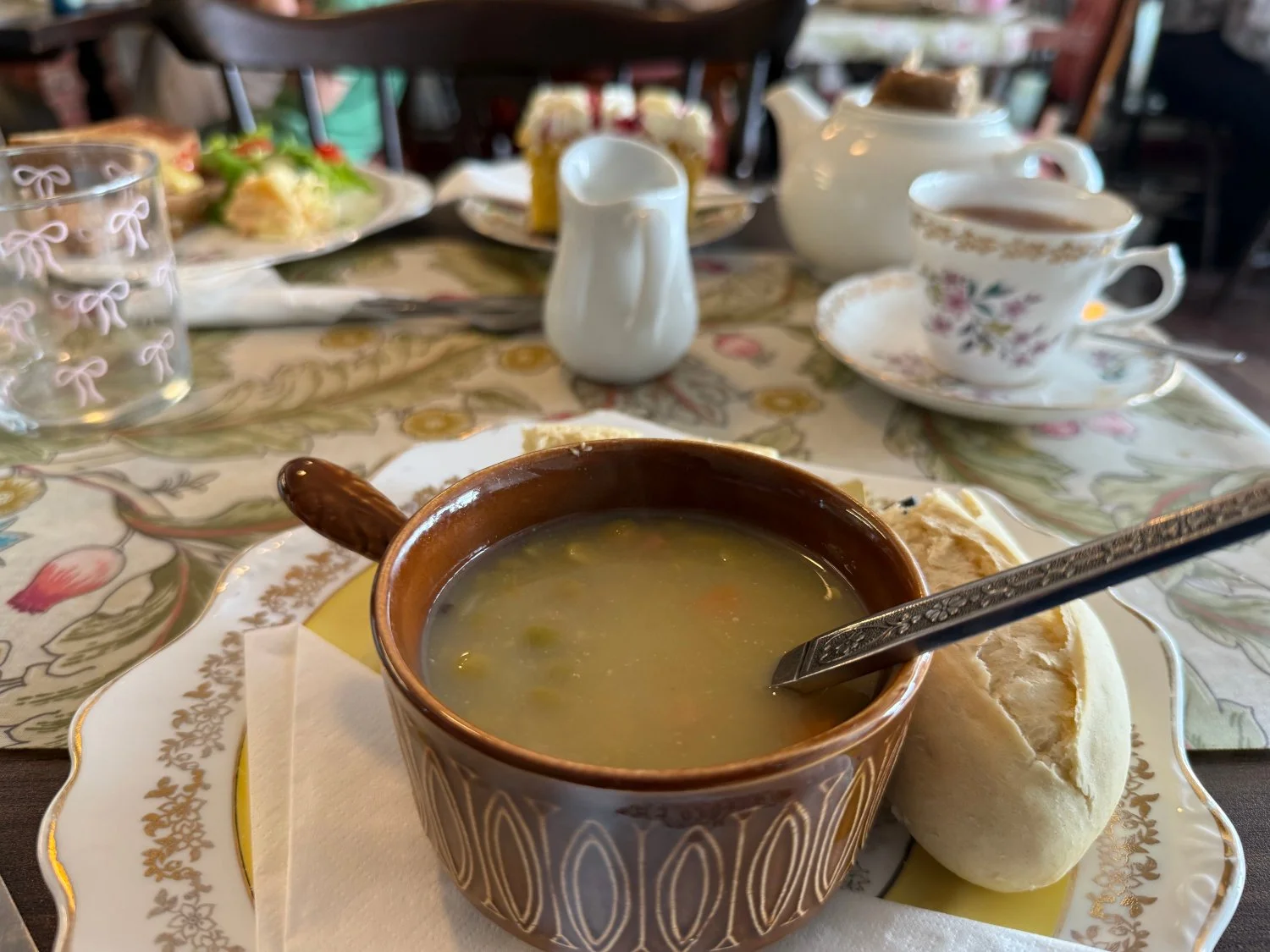 A bowl of green ham and pea soup served on a table at the Remember Me Tea Rooms in Stockton, accompanied by a toasted cheese sandwich, a slice of Victoria sponge cake, and a hot cup of tea.