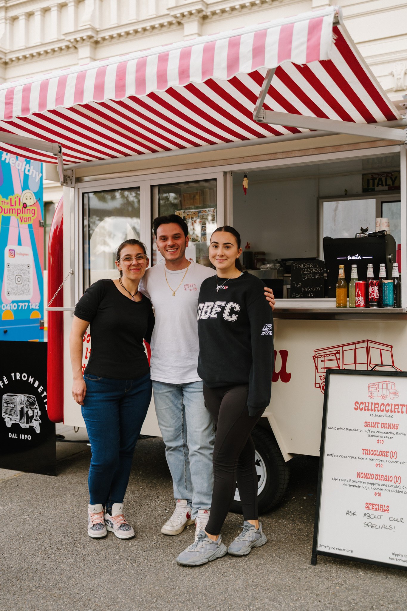 Three people standing in front of a food truck, smiling for the photo.