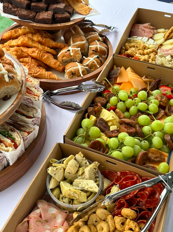 An assortment of snacks including green grapes, cheese, crackers, cured meats, prosciutto sandwiches, croissants, Italian biscuits, fresh antipasto