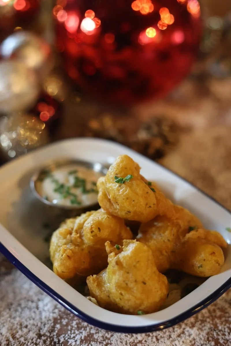 Fried pakoras in a dish with dipping sauce, garnished with herbs, and festive decorations in the background.