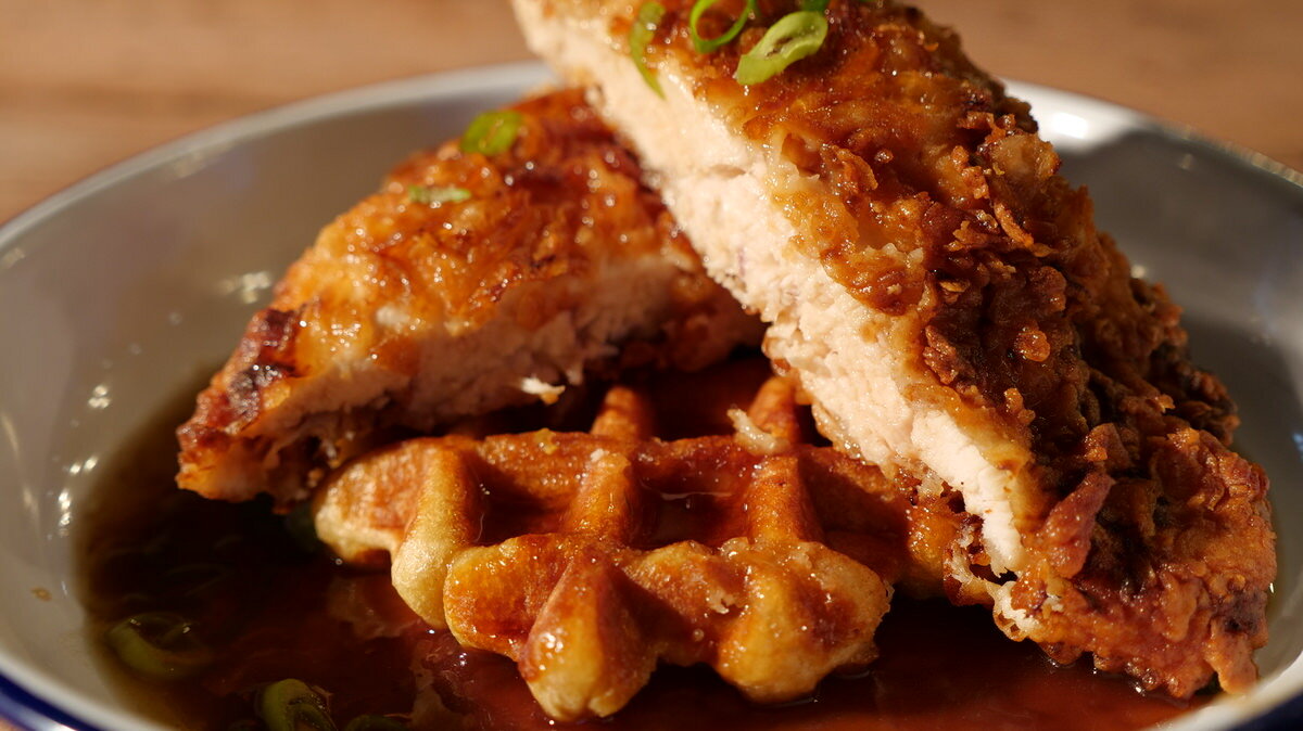 Fried chicken served on a waffle with syrup and green onions in a plate.
