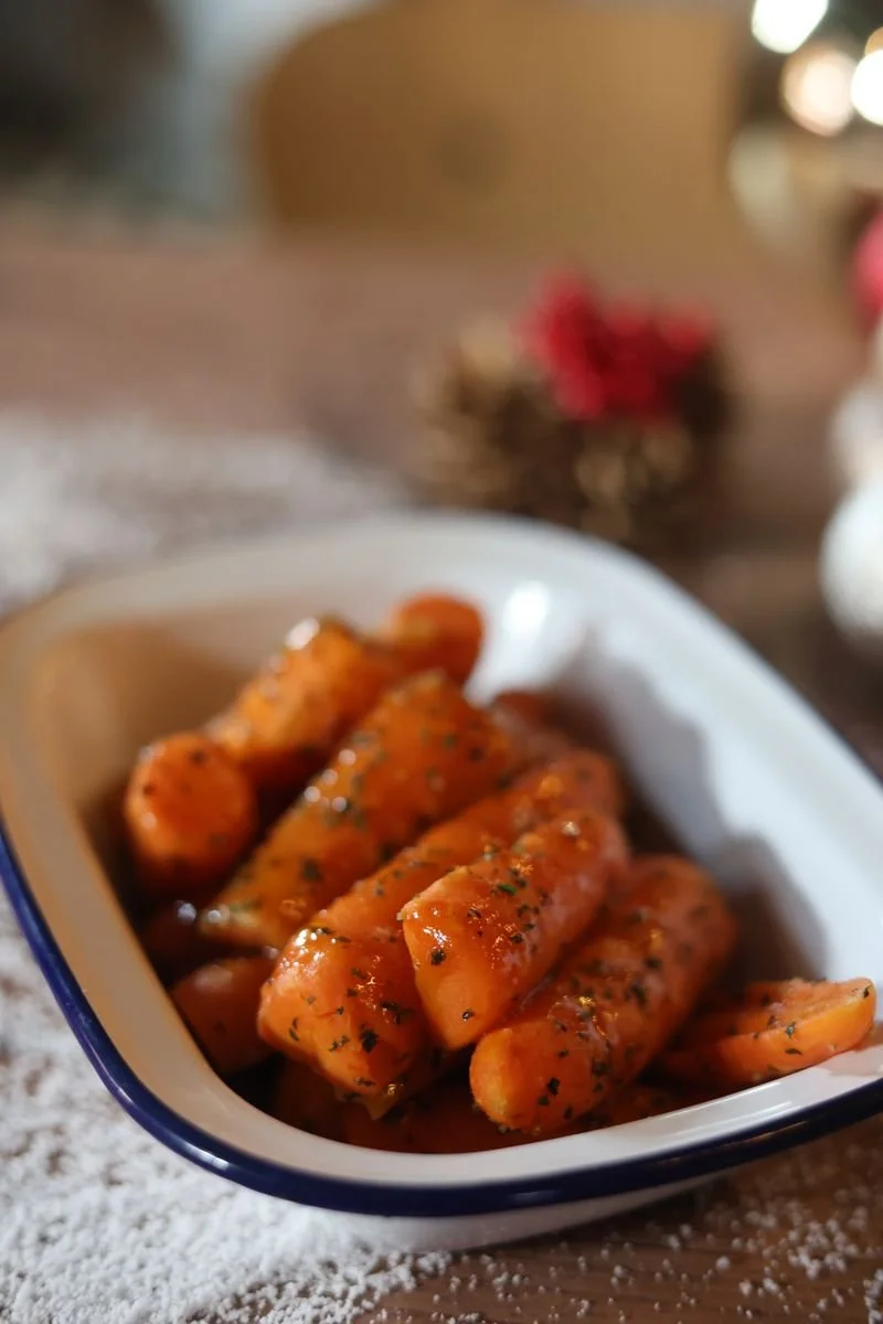 Glazed carrots with herbs in a white dish on a wooden table.