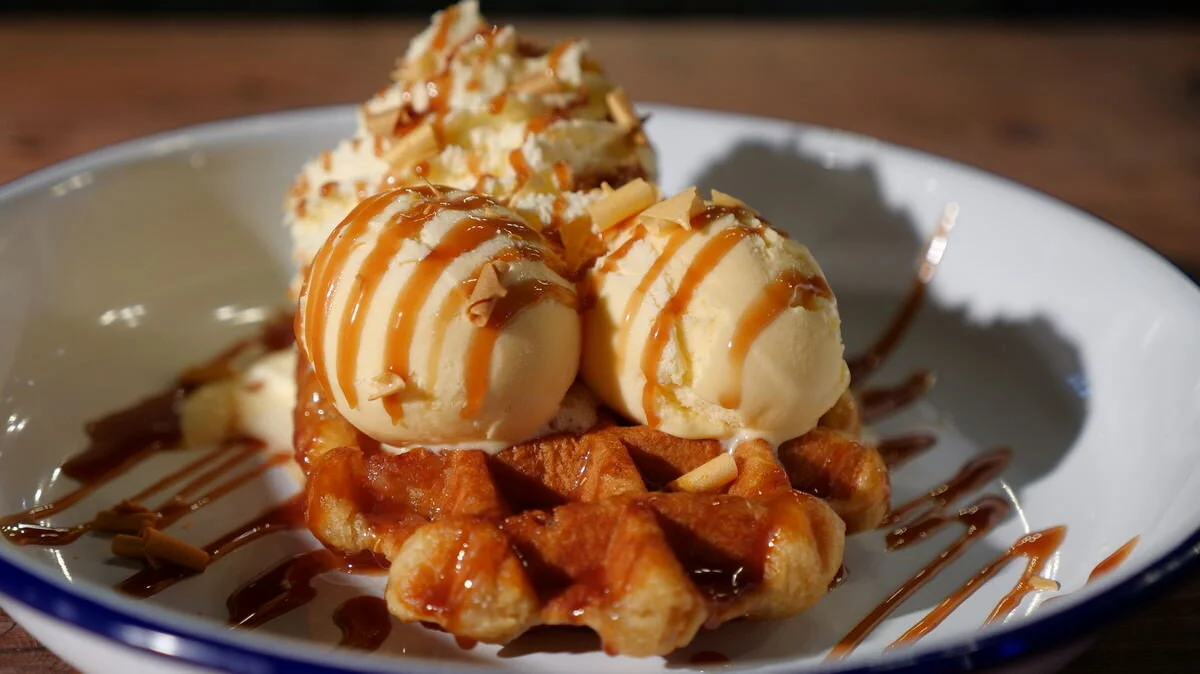 Belgian waffles with vanilla ice cream and caramel sauce in a white bowl.