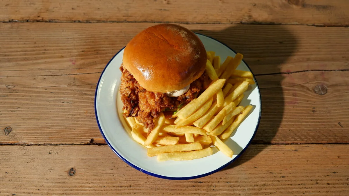 Fried chicken sandwich on a plate with French fries on a wooden table.