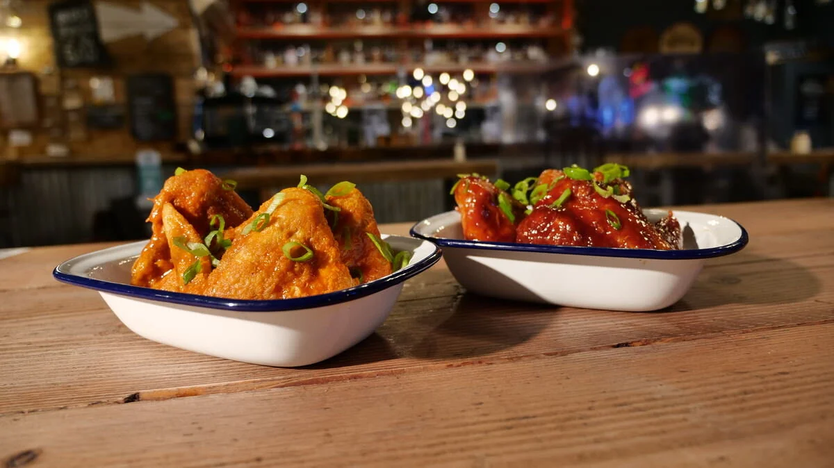 Two trays of Van Winkle chicken wings with sauces and green onions on a wooden table.