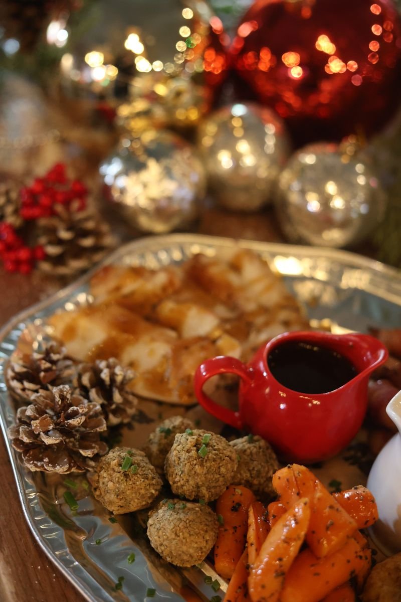 Holiday platter with festive decorations, featuring roasted vegetables, meatballs, pinecones, and shiny ornaments.