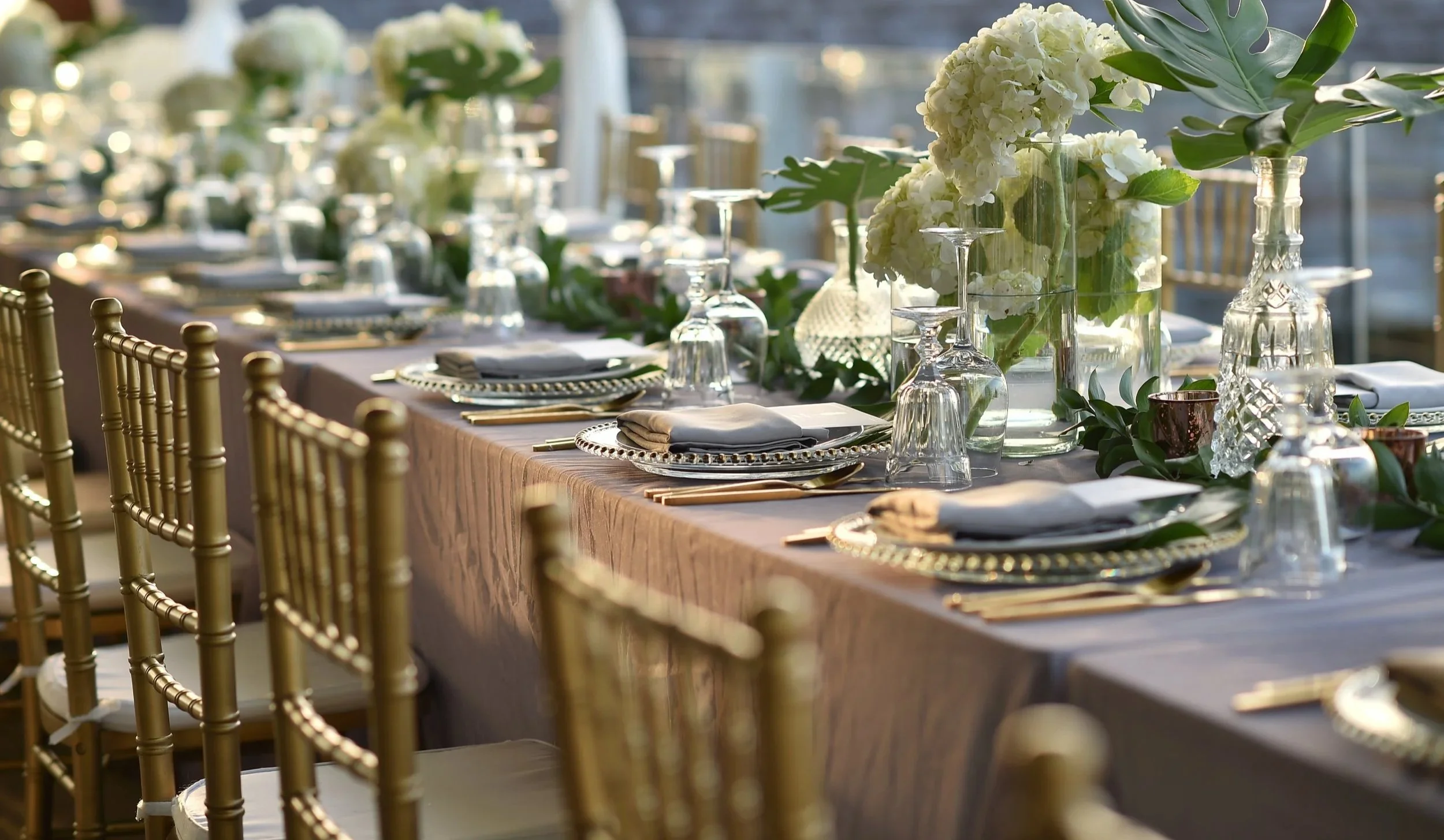 Elegant banquet table with gold chairs, floral centerpieces in glass vases, and set tableware.