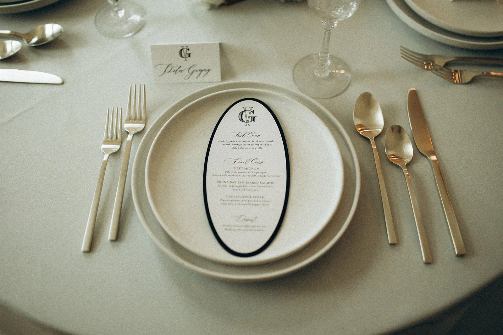 Elegant table setting with gold flatware, a white plate, a printed menu, and a place card with the name Peter Gogg.