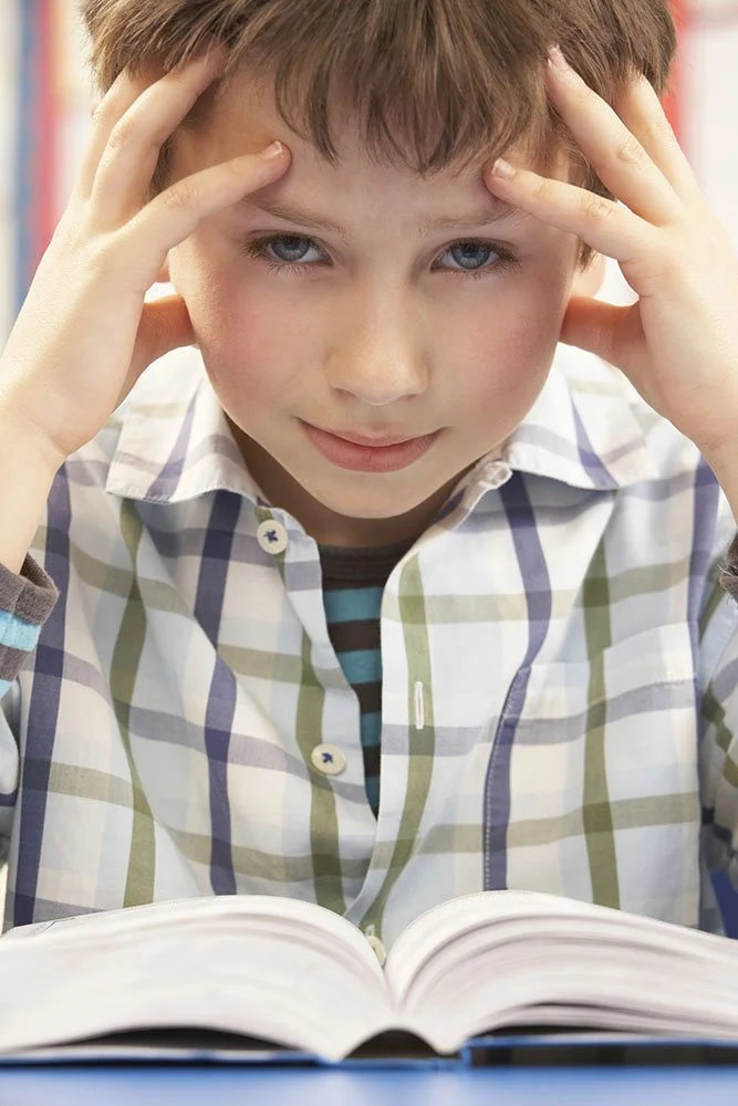 Picture of a boy wearing a plaid shirt with his head in his hands on the verge of crying because he is struggling with school