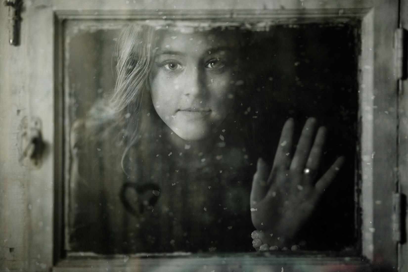 Black and white photo of a woman behind an old window with her hand against the window