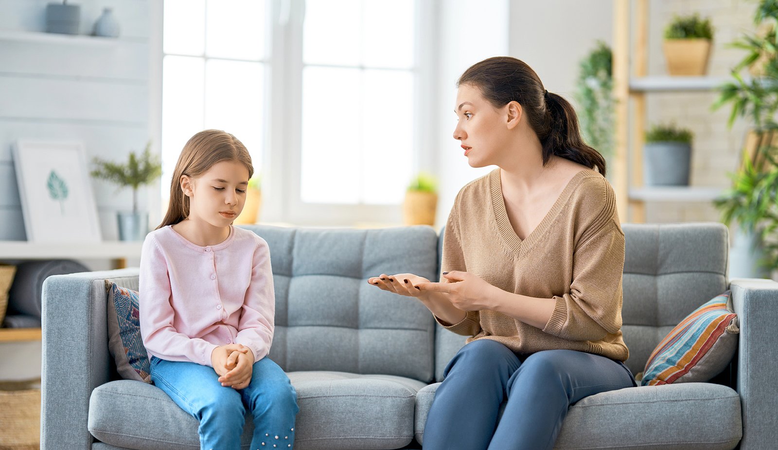 A photo of a mother scholding her child. They are setting on a gray couch.