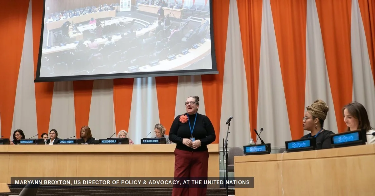 Maryann Broxton speaking at a panel in a United Nations conference room with orange and white curtains behind her
